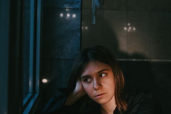 Person sitting calmly in a well-lit room, looking out a window.